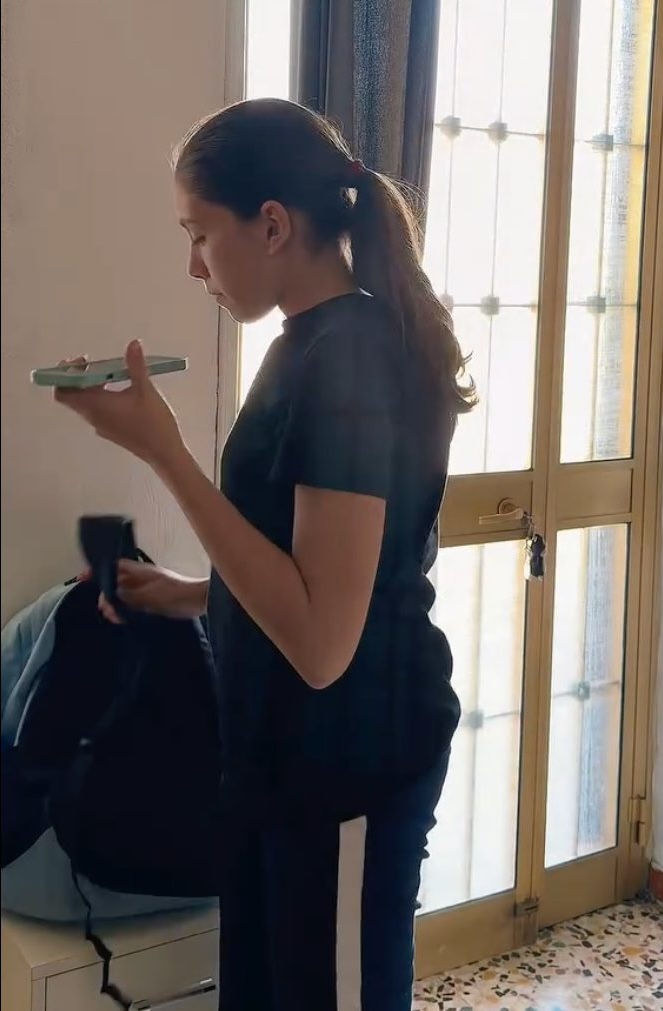 Eleonora, con lo zaino ancora addosso, ascolta il messaggio vocale del pap&agrave; al telefono vicino alla finestra
